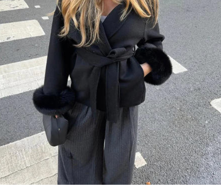 Woman in a black coat with fur trim standing on a street